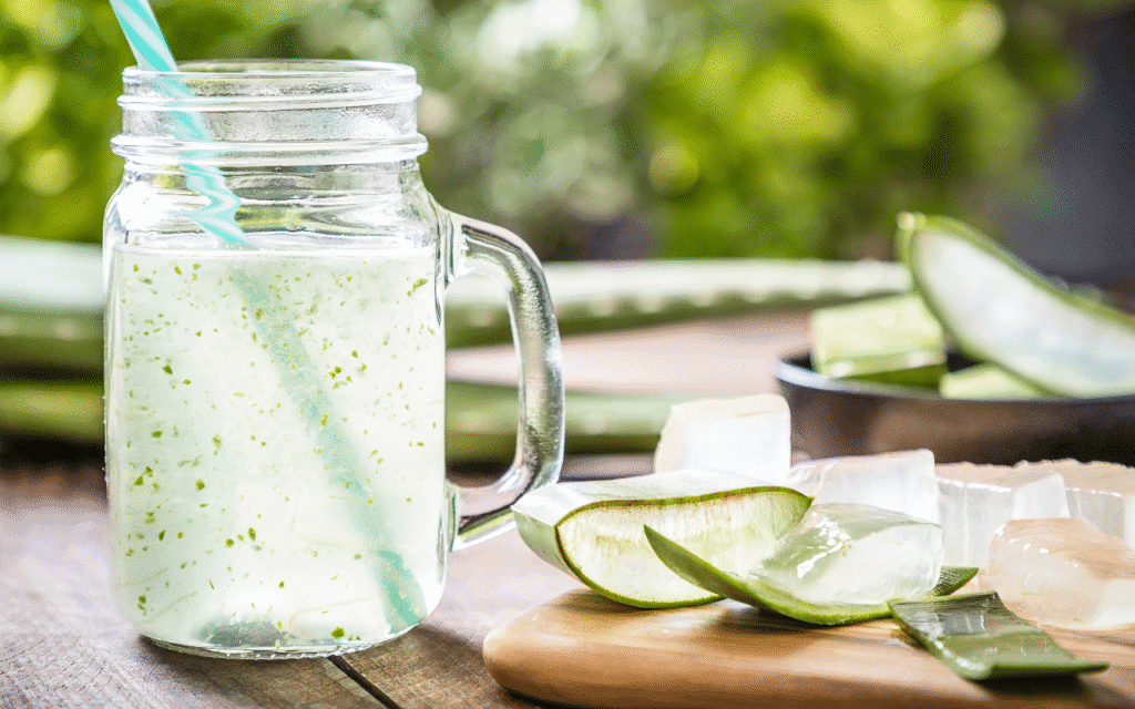 Sklenice aloe vera šťávy s ledem a čerstvě rozříznutými listy aloe na dřevěném prkénku